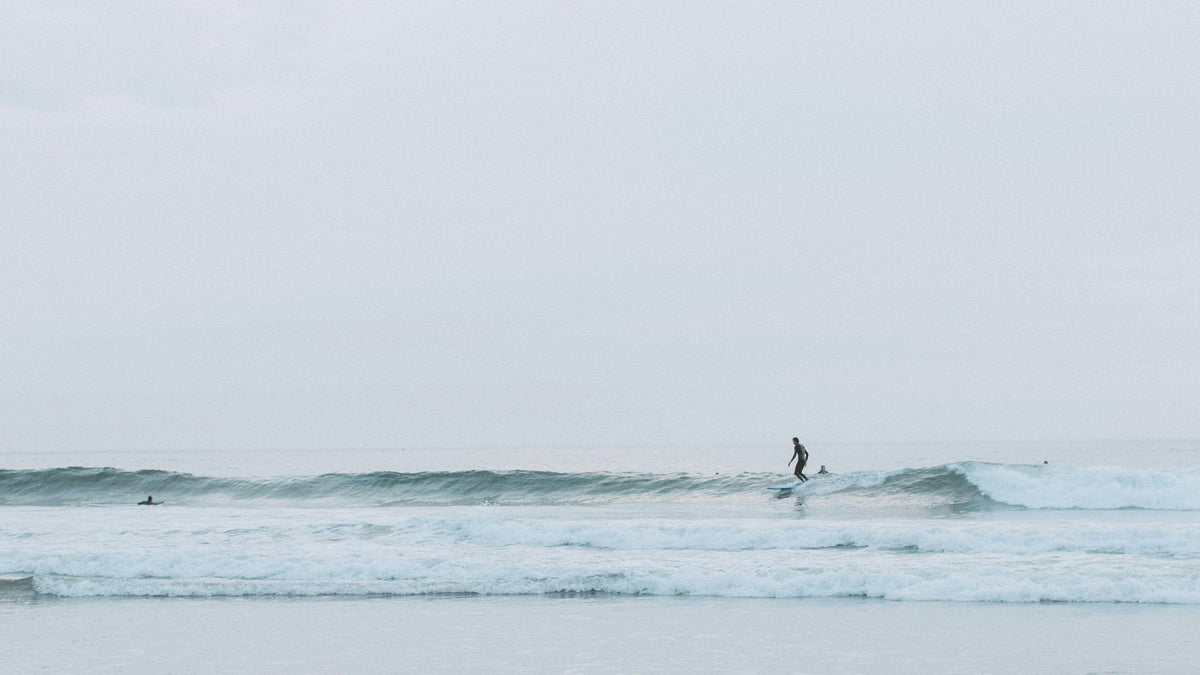 Person surfing on a calm body of water with a light blue sky.