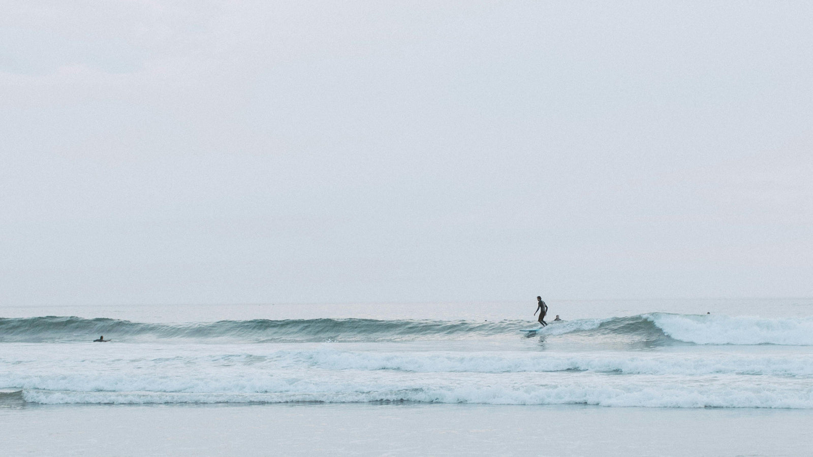 Person surfing on a calm body of water with a light blue sky.