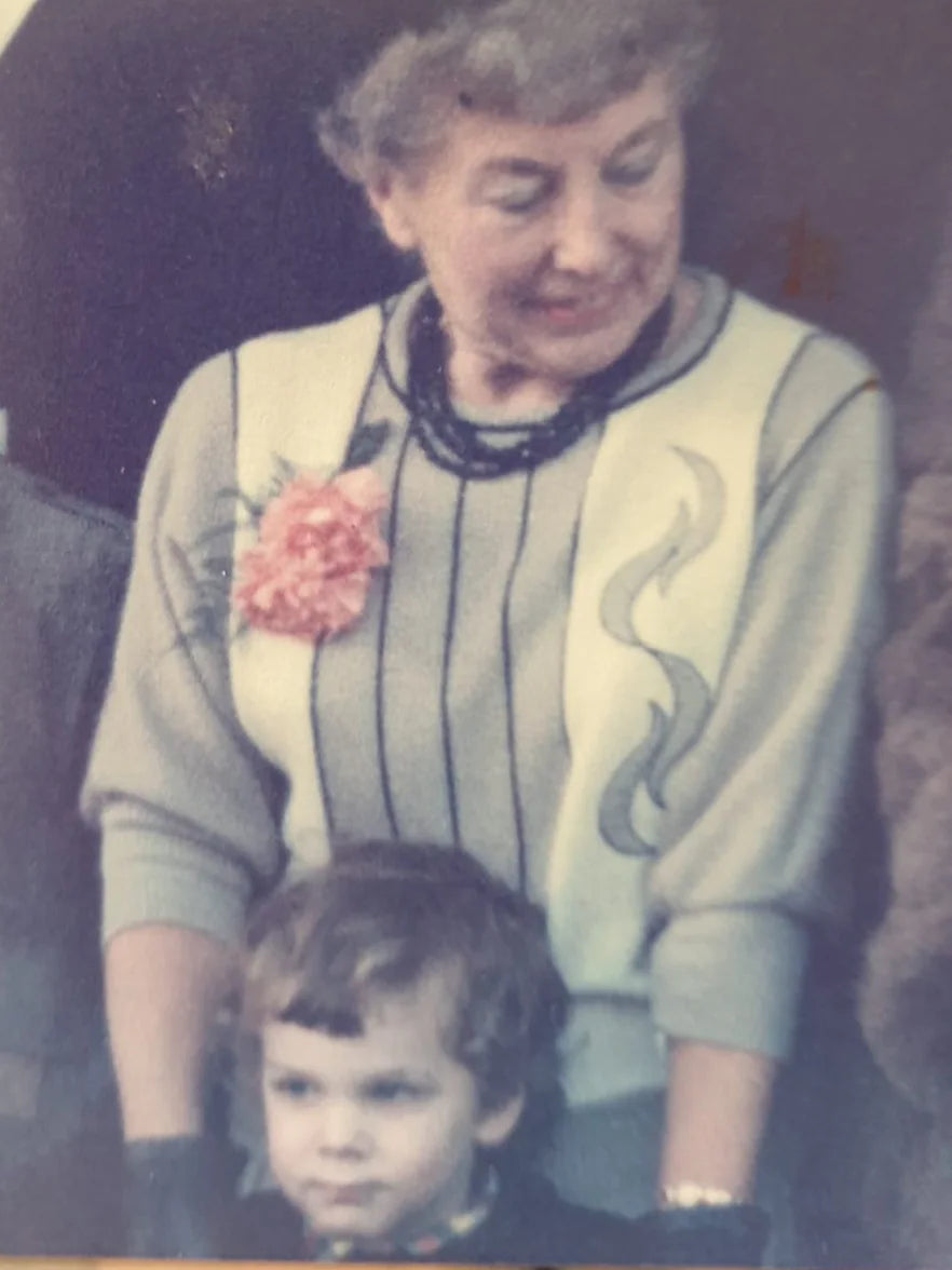 One of our nans in a patterned jumper with a pink flower pinned to it, smiling down at a little one.